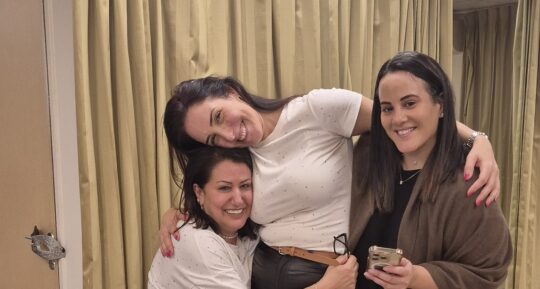 שלוש חברות צוחקות ומתחבקות בערב נשים לבחור בשמחה