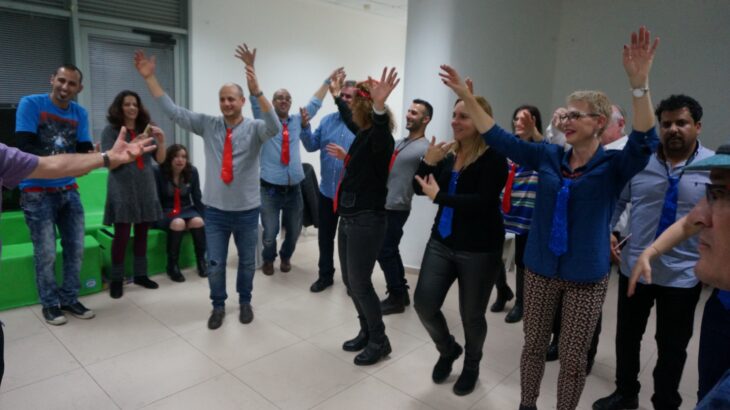 עובדים בערב צוות מרימים ידיים בפעילות קבוצתית באולם החברה