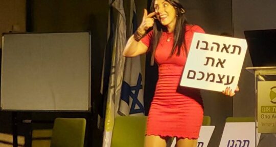 הילה עשור עם שלט "תאהבו את עצמכם"