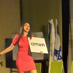 הילה עשור רוקדת על הבמה עם שלט "תצחקו"