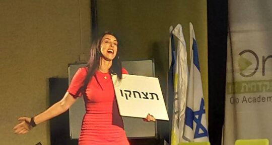 הילה עשור רוקדת על הבמה עם שלט "תצחקו"