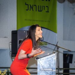 הילה עשור צוחקת ליד הפודיום בהרצאה