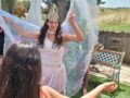 כלה עם כתר רוקדת בגינה עם כנפיים לבנות מול החברות