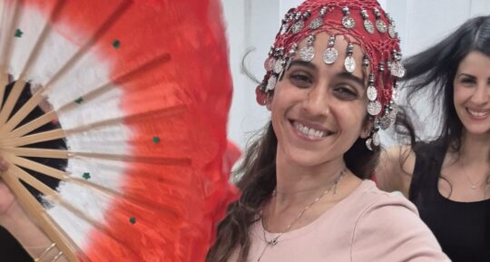 אישה מחייכת עם כיסוי ראש מטבעות ומניפה אדומה בערב נשים