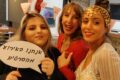 שלוש חברות מחייכות עם שלט 'אנחנו באירוע מהסרטים' ואוזני ארנב